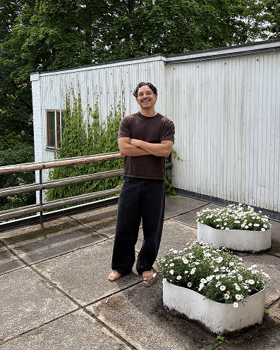 Dennis Valencia står på en takterrass framför en plåtvägg, med blommor bredvid sig