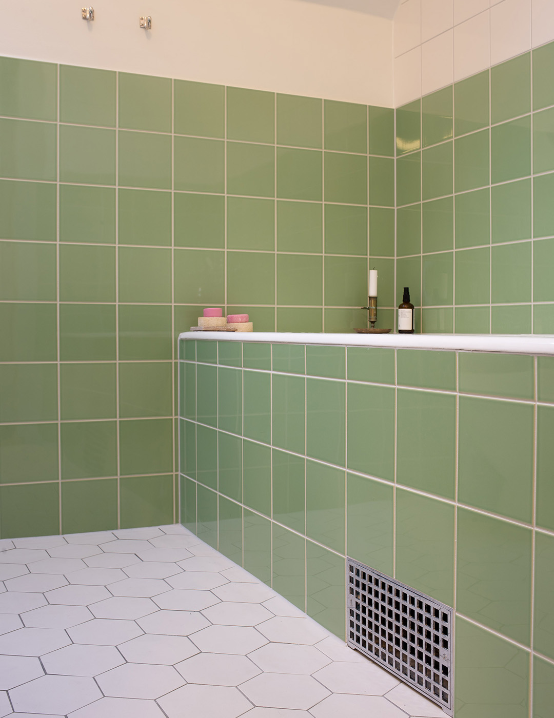 Funkisbadrum med inbyggt badkar med ljusgrönt kvadratiskt kakel satt i rakt förband. Klinkergolv av vita hexagonformade plattor.