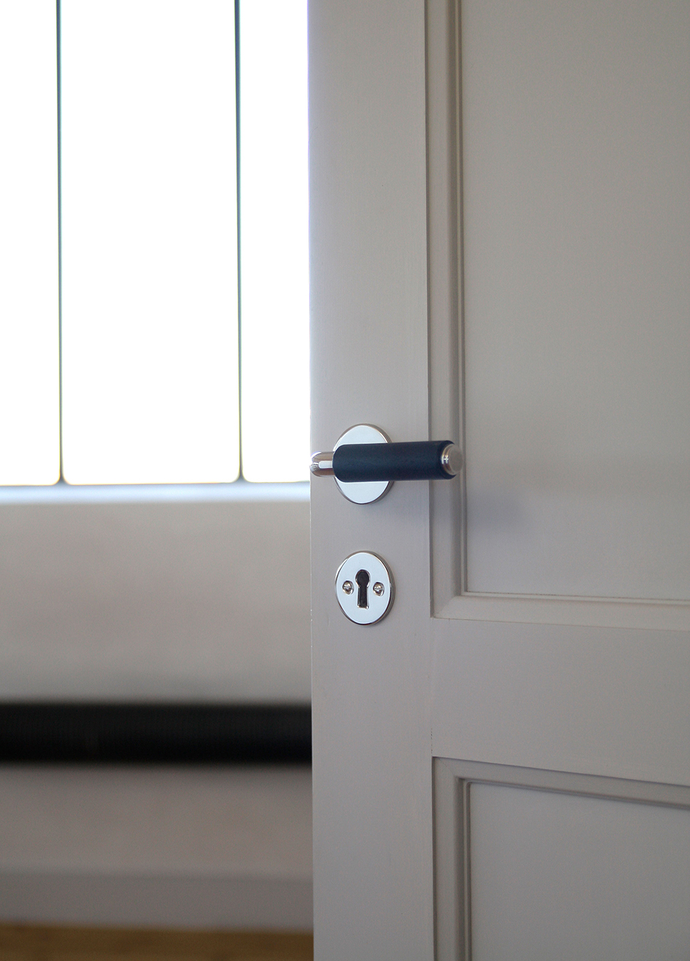 Ett funkistrycke med svart grepp, rund rosett och nyckelskylt på en ljusgrå spegeldörr i funkisstil.