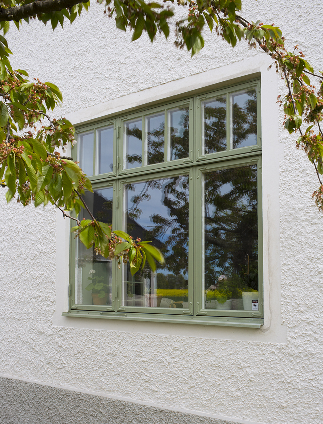 Grönt fönster som målats med linoljefärg mot en vitputsad fasad.