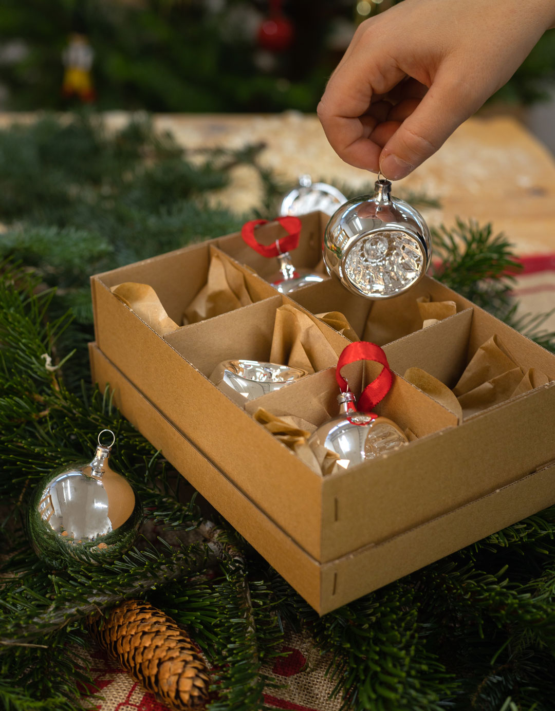 Hand tar upp en julgranskula i silver ur en kartong