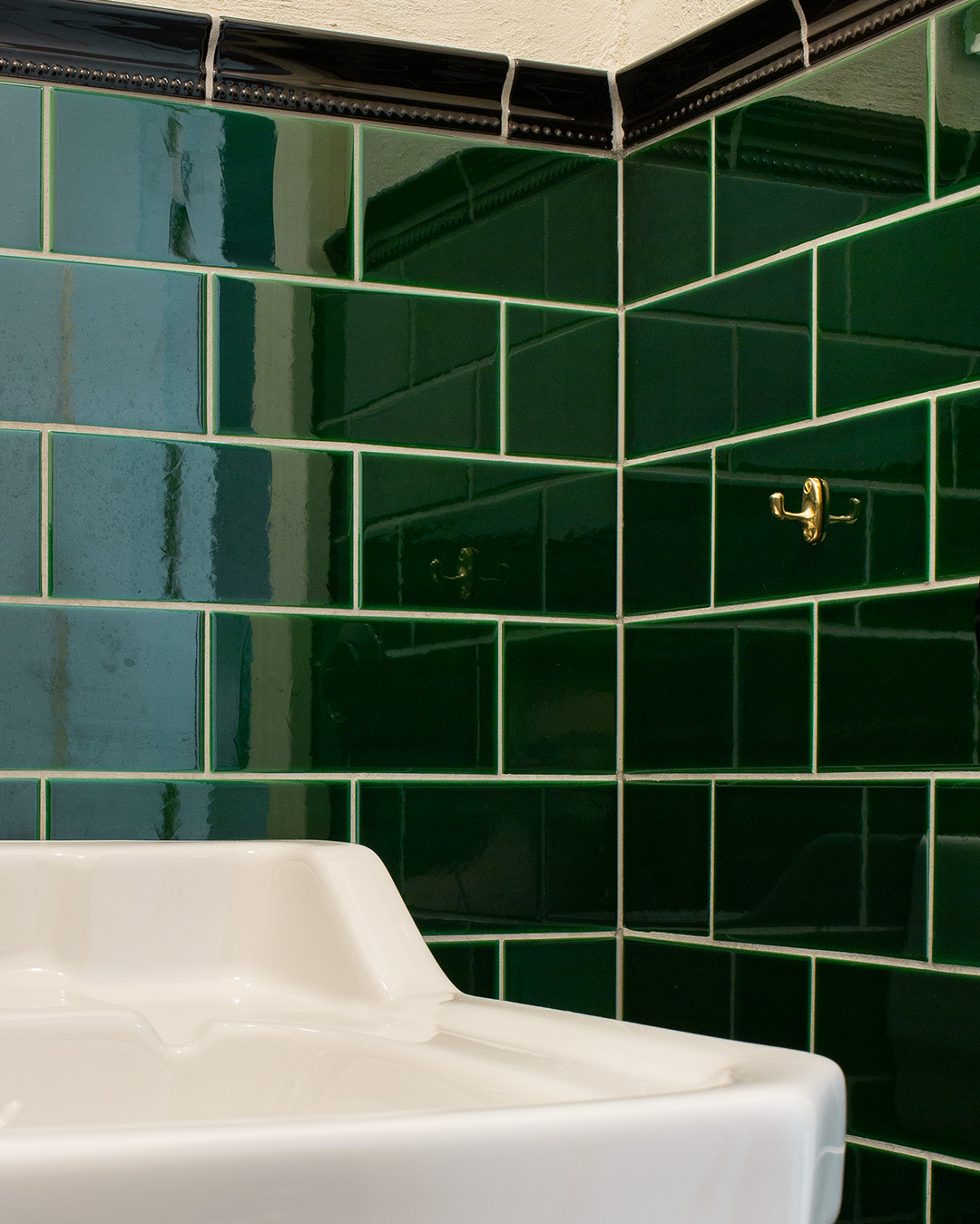Kaklat hörn i badrum med gröna plattor i half tileformat satta i tegelförband.