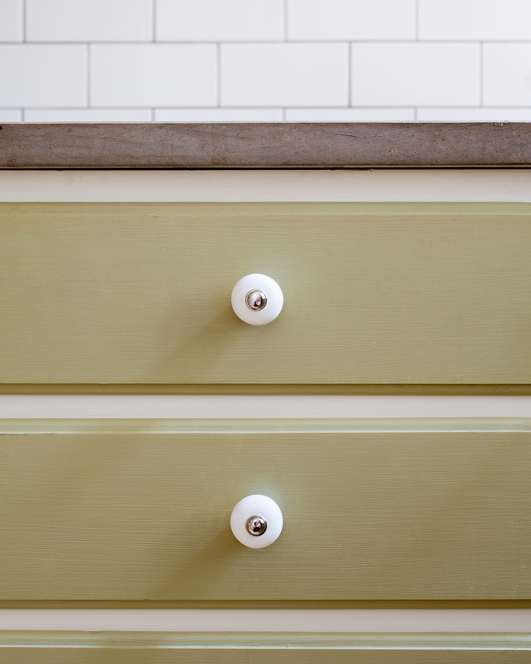 Beslag av porslin på lådor i ett måttbyggt kök målat med linoljefärg i kulören Ljus Oliv.