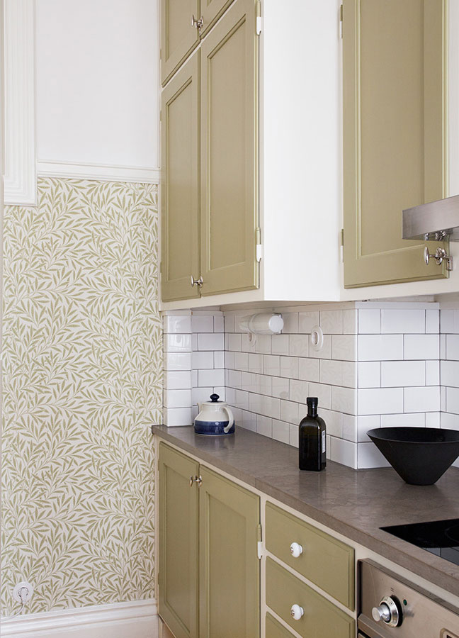 Måttbyggt kök med vita porslinsknoppar och tapetserad vägg i bakgrunden.