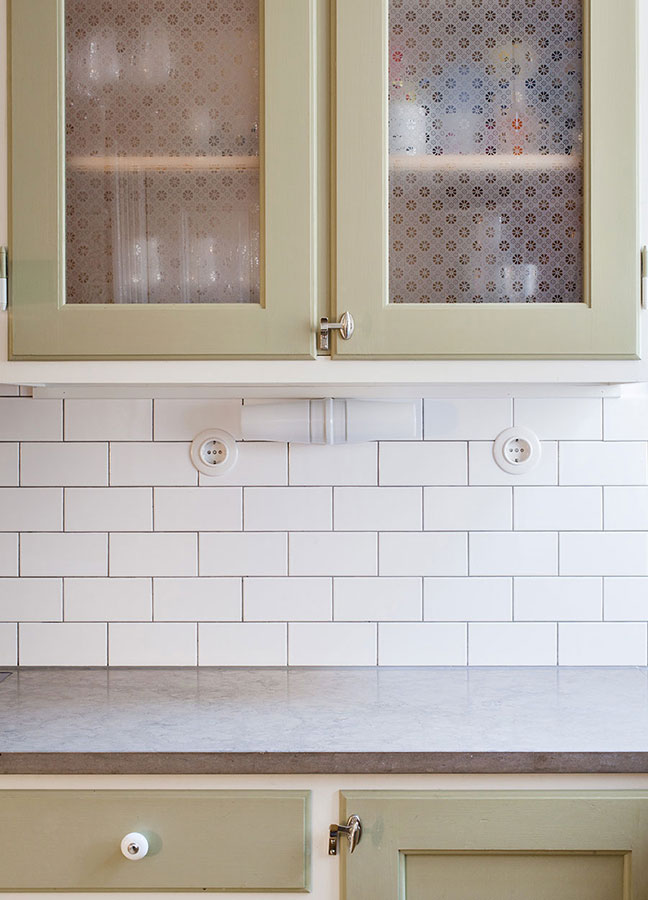 Grönmålat, måttbyggt kök med kaklad vägg av vita half tiles i tegelförband.
