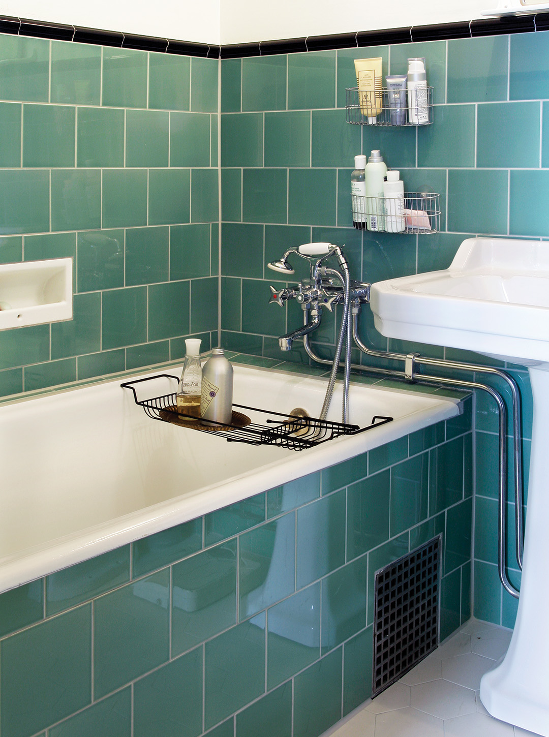 Badrum med inbyggt badkar klätt med grönblått kakel halvvägs upp på väggen. 
